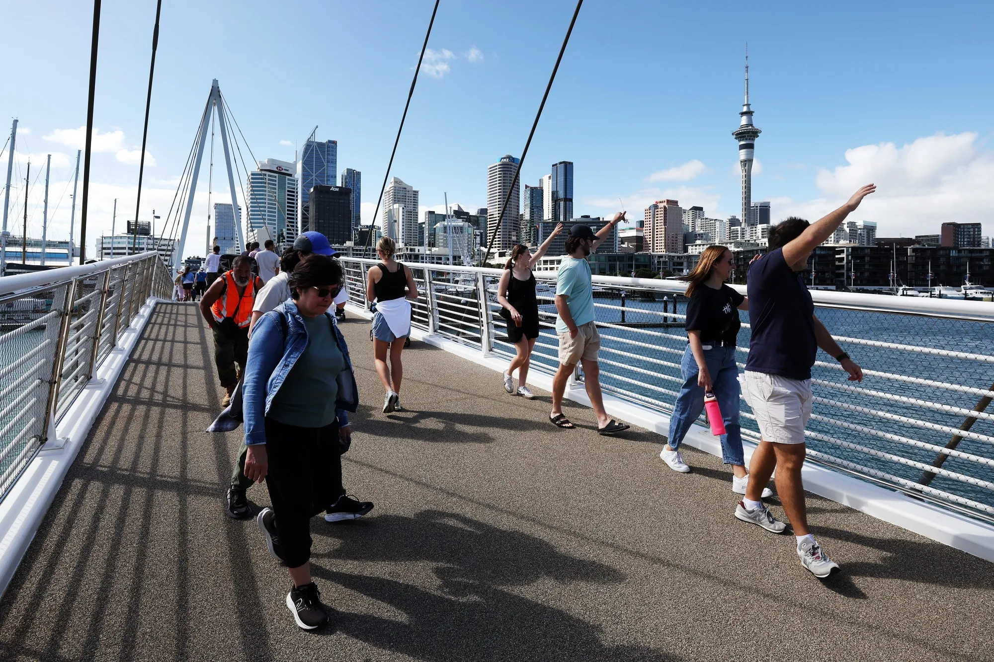 Pedestrians cross a bridge as the Sky Tower and other buildings stand in the background in Auckland, New Zealand.