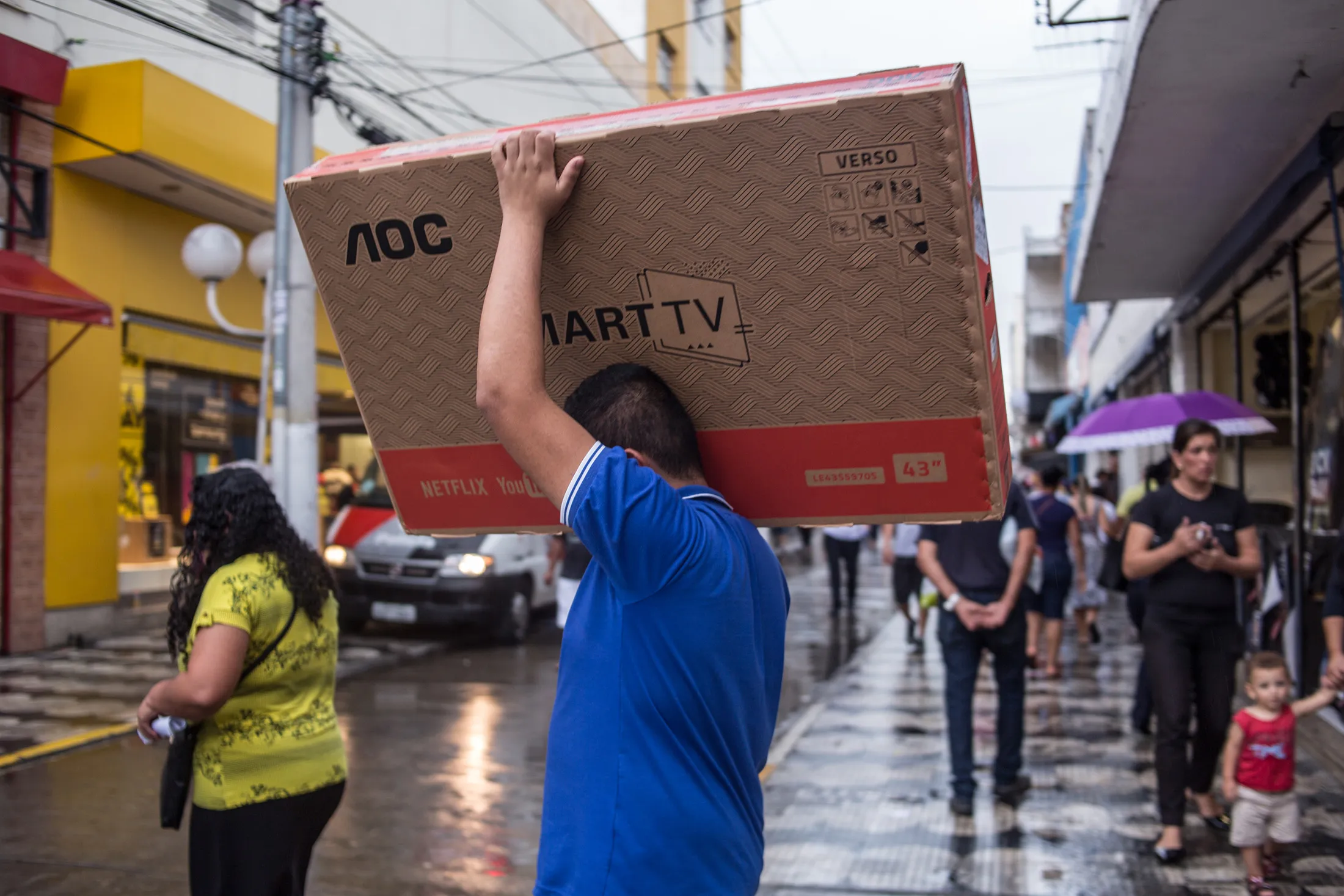 A man crosses the street with a new TV on his shoulder in Sao Paulo, Brazil.