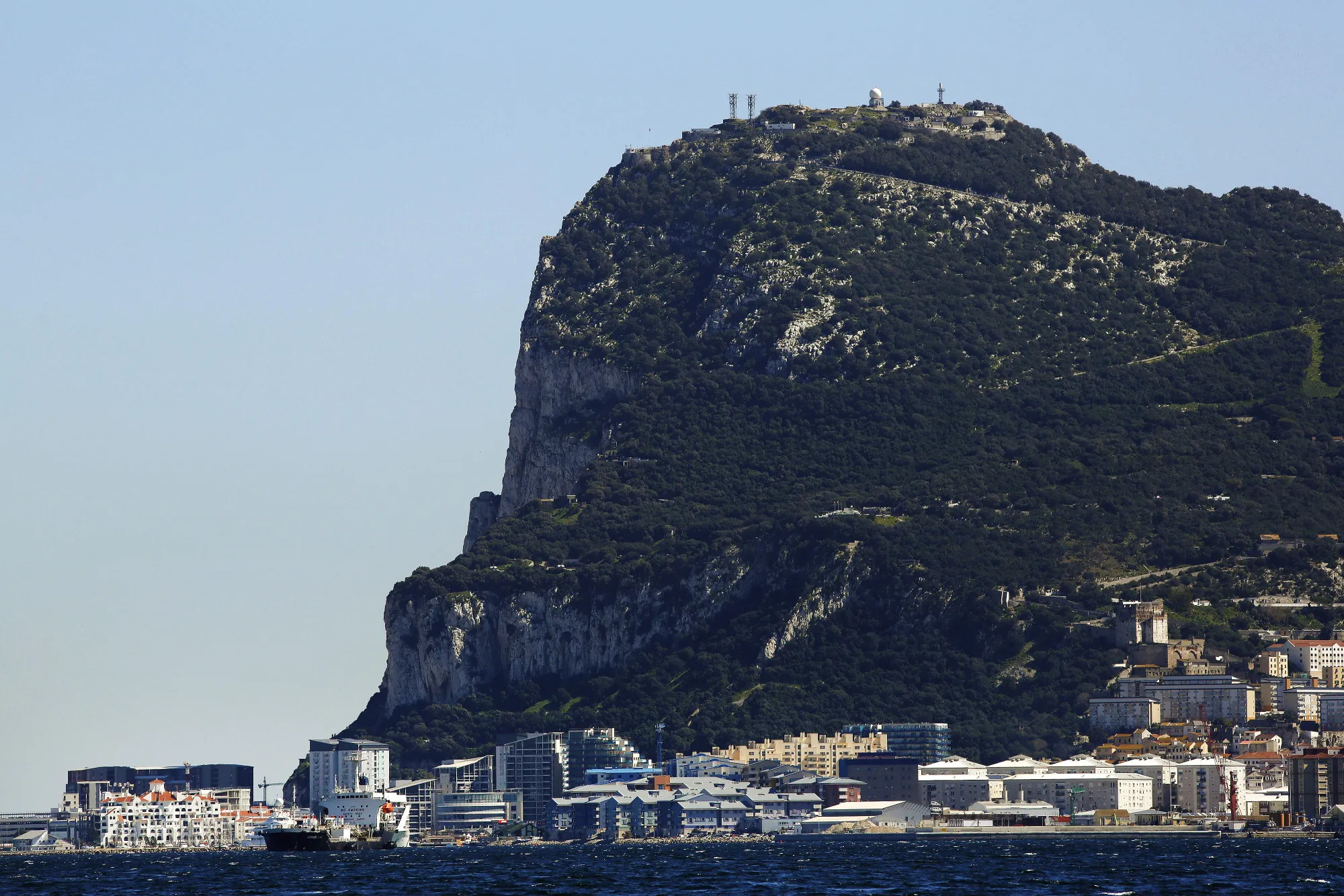 Commercial and residential buildings stand along the waterline at the base of the rock of Gibraltar.