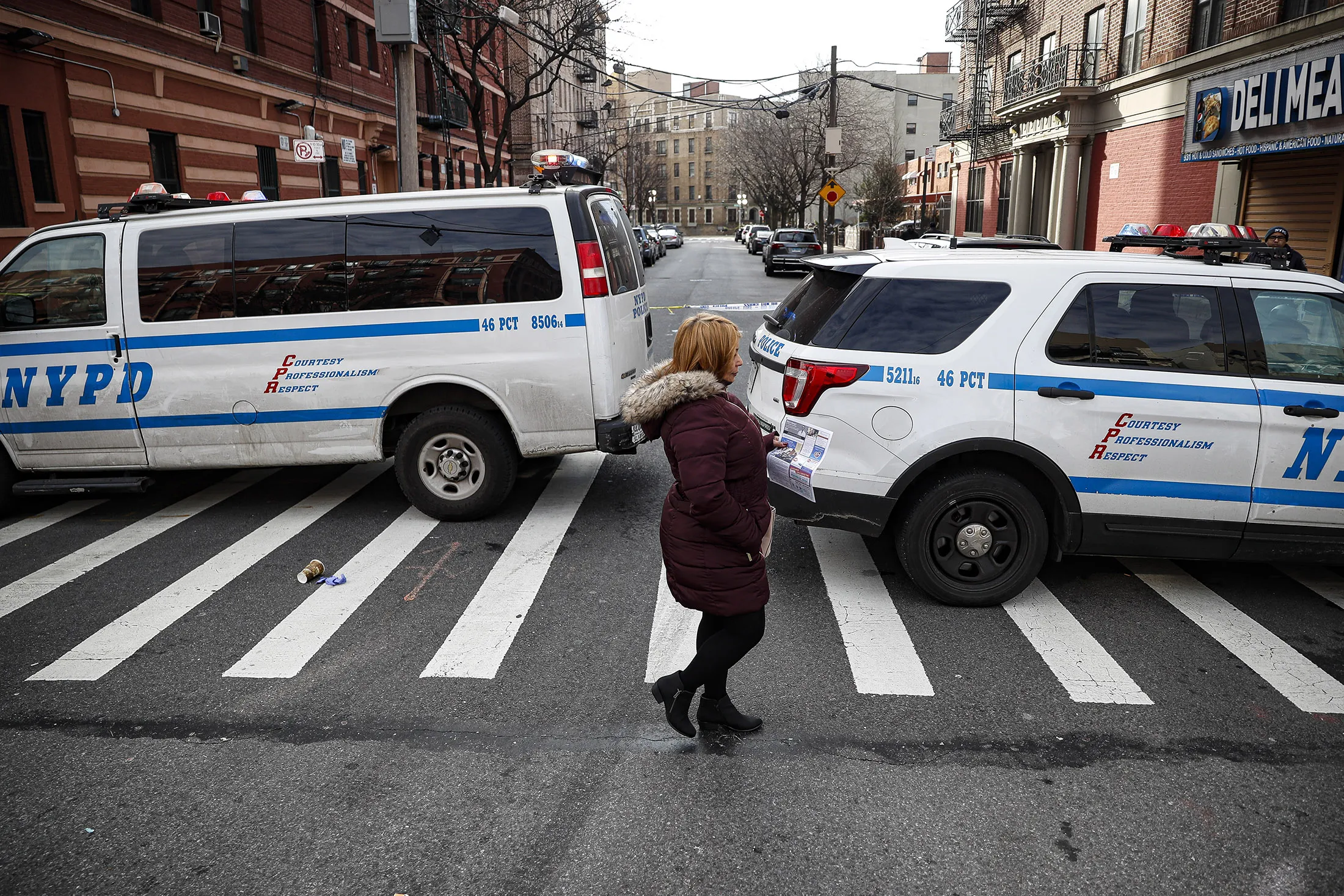 A woman walks past New York City police vehicles near the scene of a police involved shooting in the Bronx on Feb. 9.