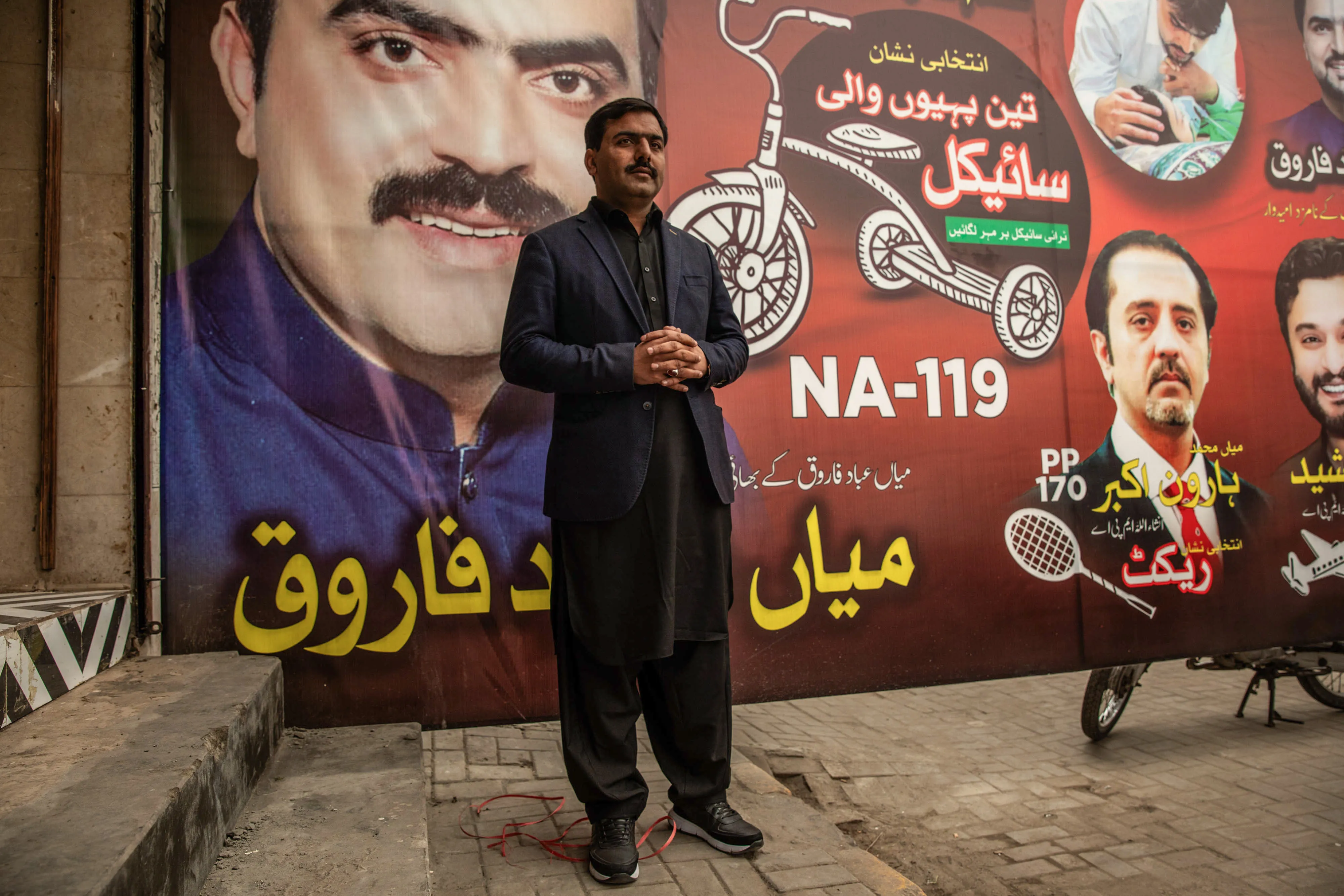 Tasawar Farooq in front of a campaign poster that includes his brother, candidate Shahzad Farooq, in Lahore on Jan. 25.