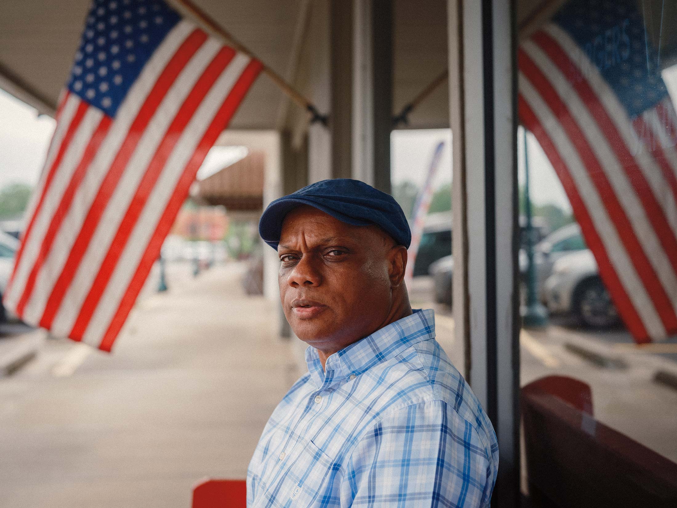A portrait of Floyd McDade at E.W. Thomson Drug Co. in Delhi, Louisiana, one of the town centers of Richland Parish. A giant American flag hangs in the background.