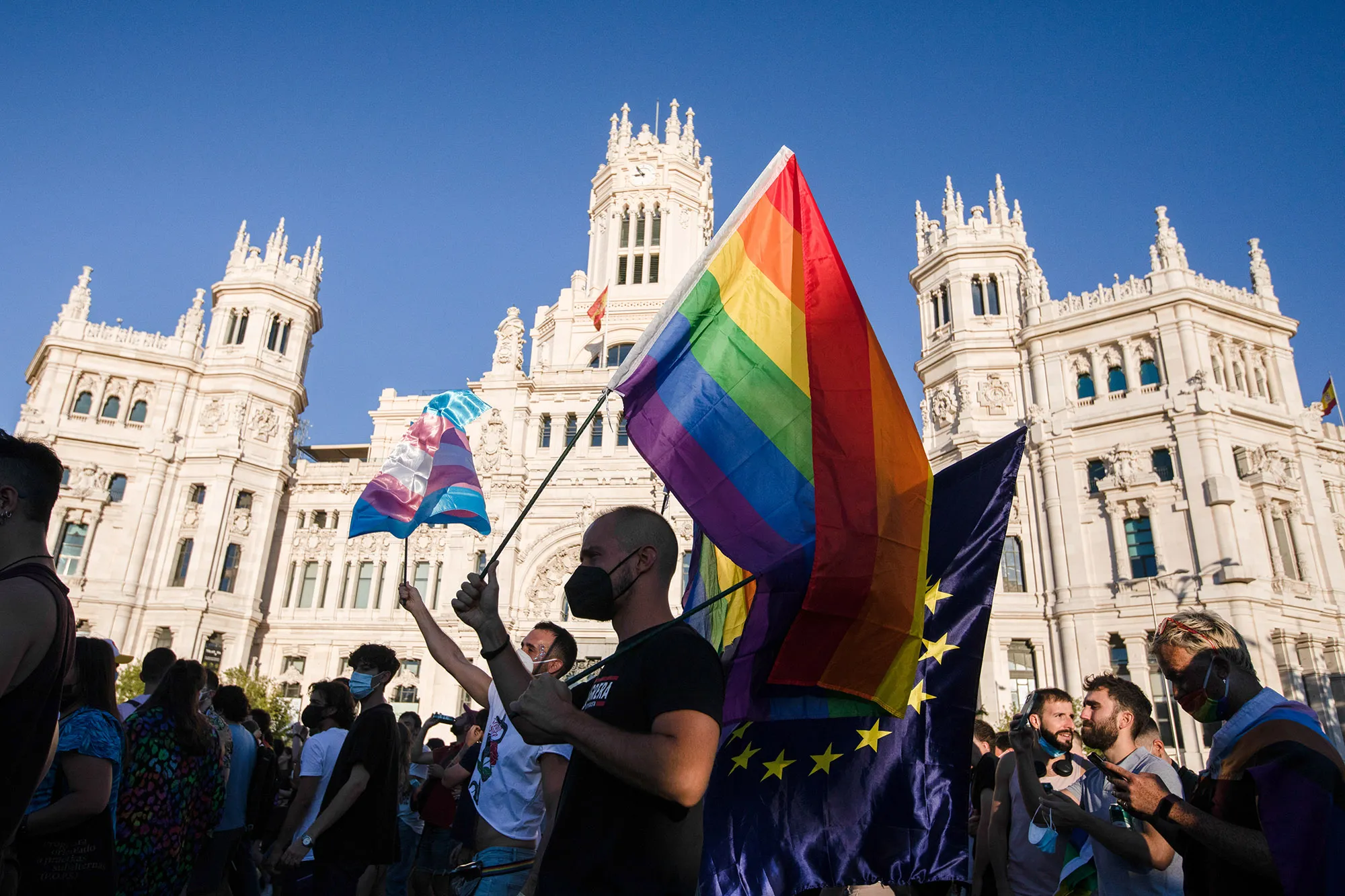 Demonstrators waves a rainbow flag and a trans flag during