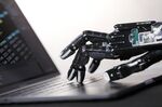 A robotic hand touches the keyboard of a laptop computer.