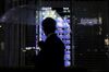 A pedestrian holding an umbrella walks past an illuminated electronic stock board displayed outside the Daiwa Securities Co. headquarters at night in Tokyo, Japan, on Monday, July 27, 2020. Daiwa Securities is schedule to announce first-quarter earning figures on July 31.