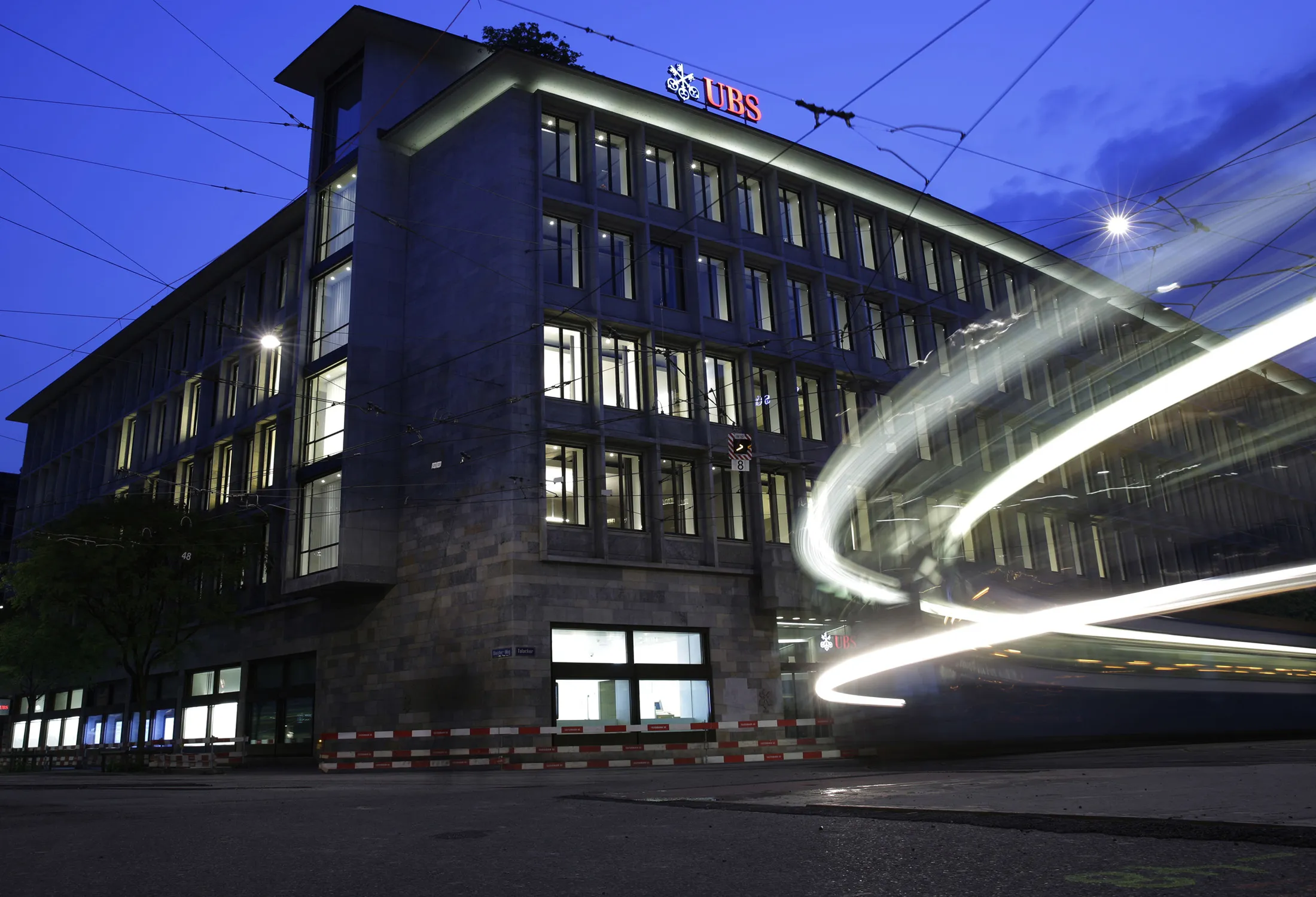 A sign sits illuminated on the roof of the UBS Group AG headquarters as light trails are left by moving traffic in this long exposure photograph taken in Zurich.

