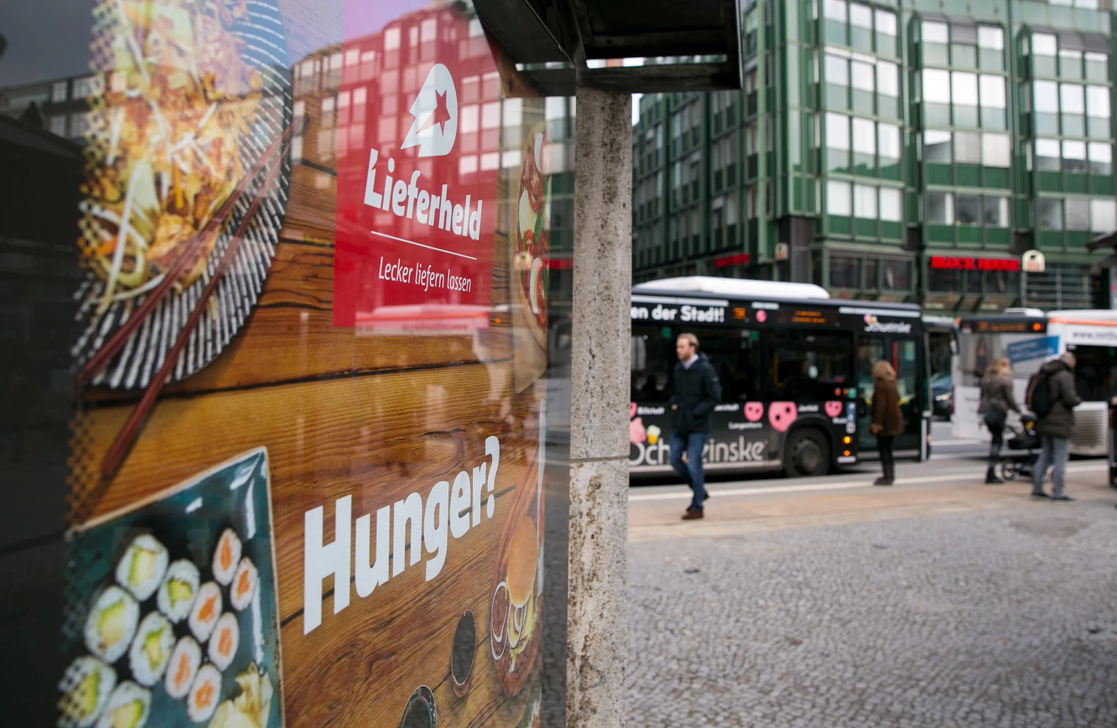 Pedestrians and buses pass a Delivery Hero advertisement on a street in Hamburg.
