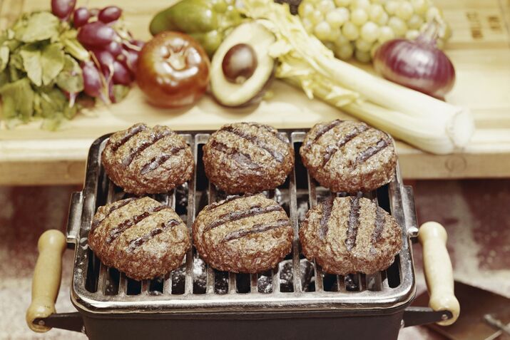 Roasted meat on grill with vegetable in background, close-up