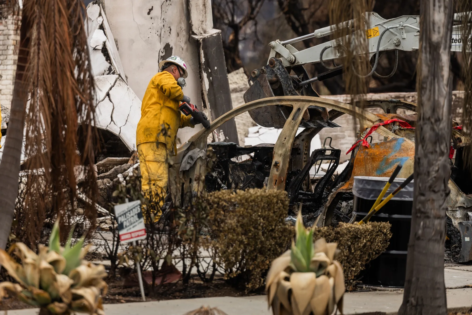 Cleanup workers cut apart an electric vehicle in the Pacific Palisades.