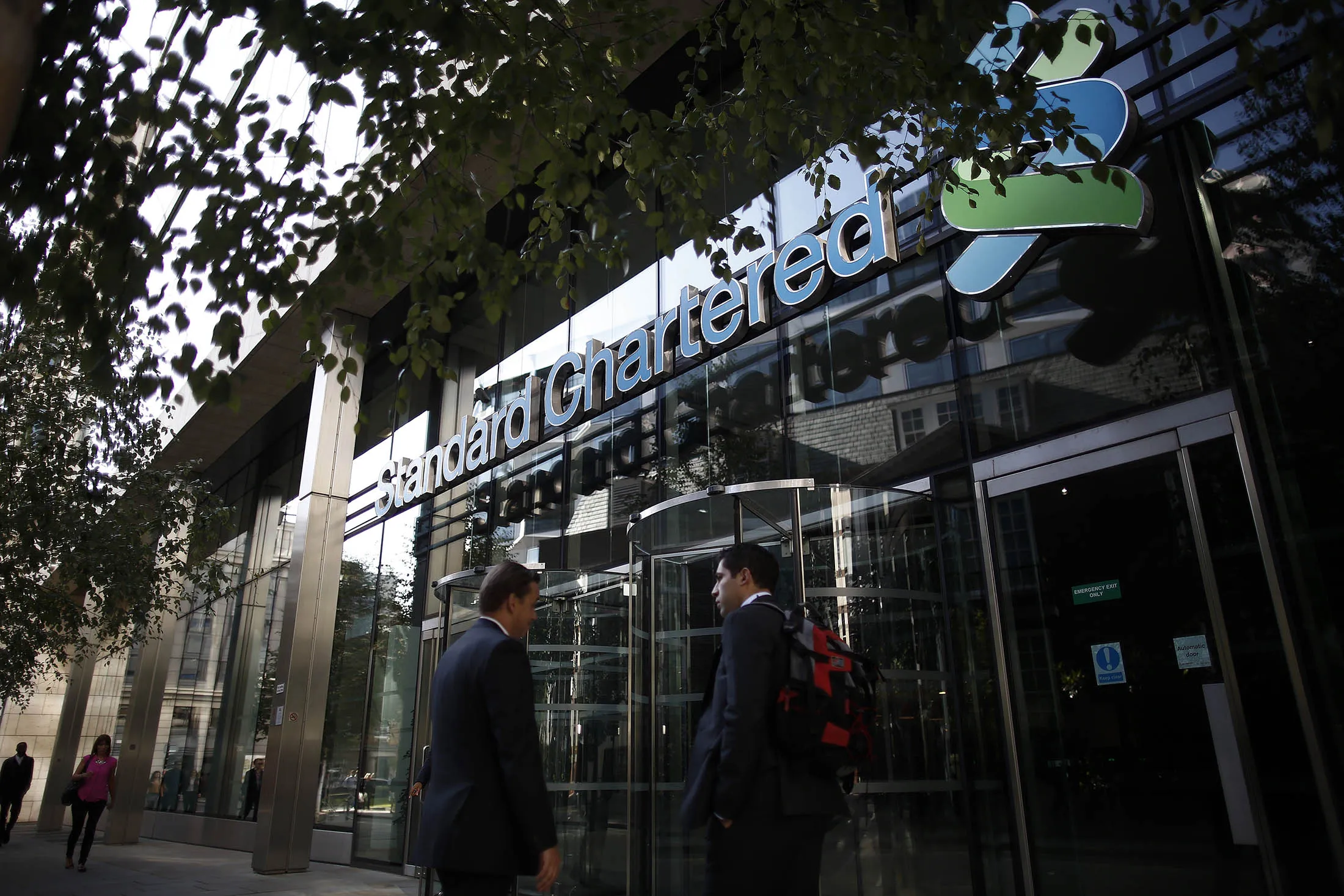 Pedestrians walk past the entrance to Standard Chartered's headquarters in London.
