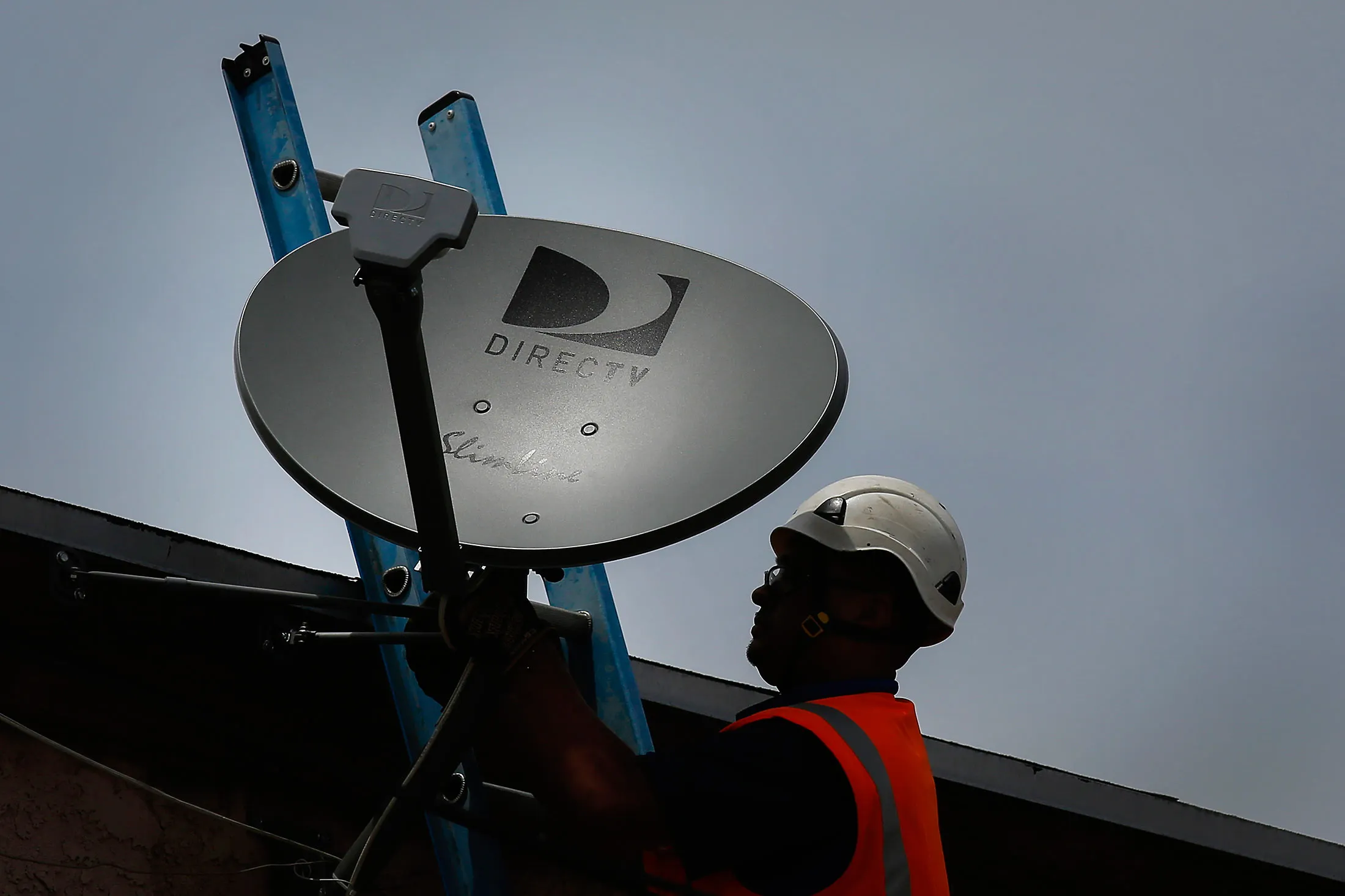 A DIRECTV technician installs a new satellite TV dish at an apartment building in Lynwood, California, U.S., on Monday, May 5, 2014.

