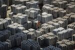 A worker stands among bundles of aluminum ingots sitting stacked at a stockyard in Wuxi, China.