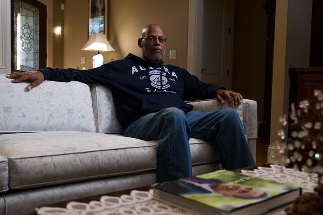 Portrait of Tony Grice on a couch at his home with a book on his coffee table in the foreground picturing Barack Obama on the cover. 