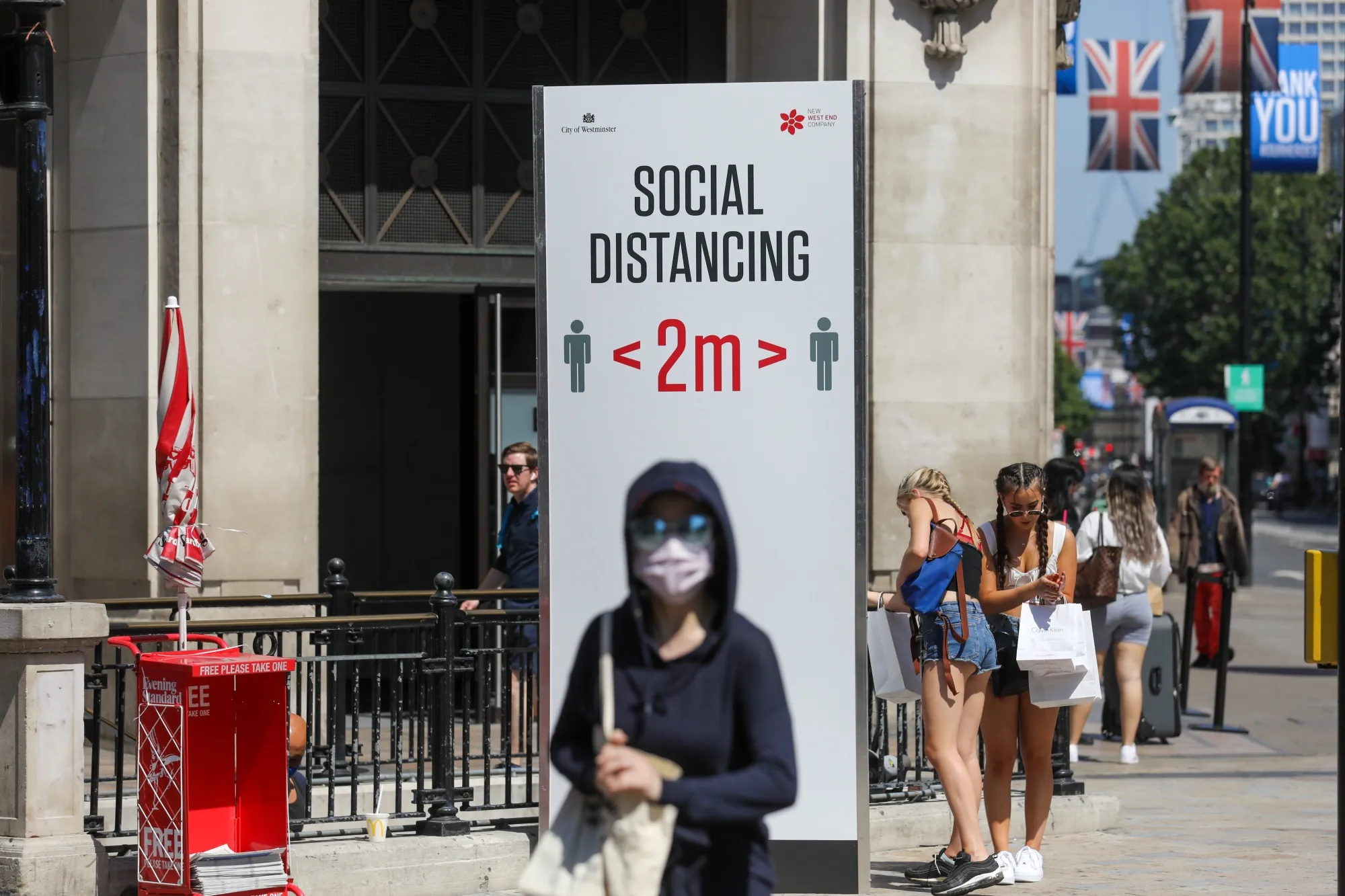 A pedestrian wearing a protective face mask as she passes a social distancing sign in central London.