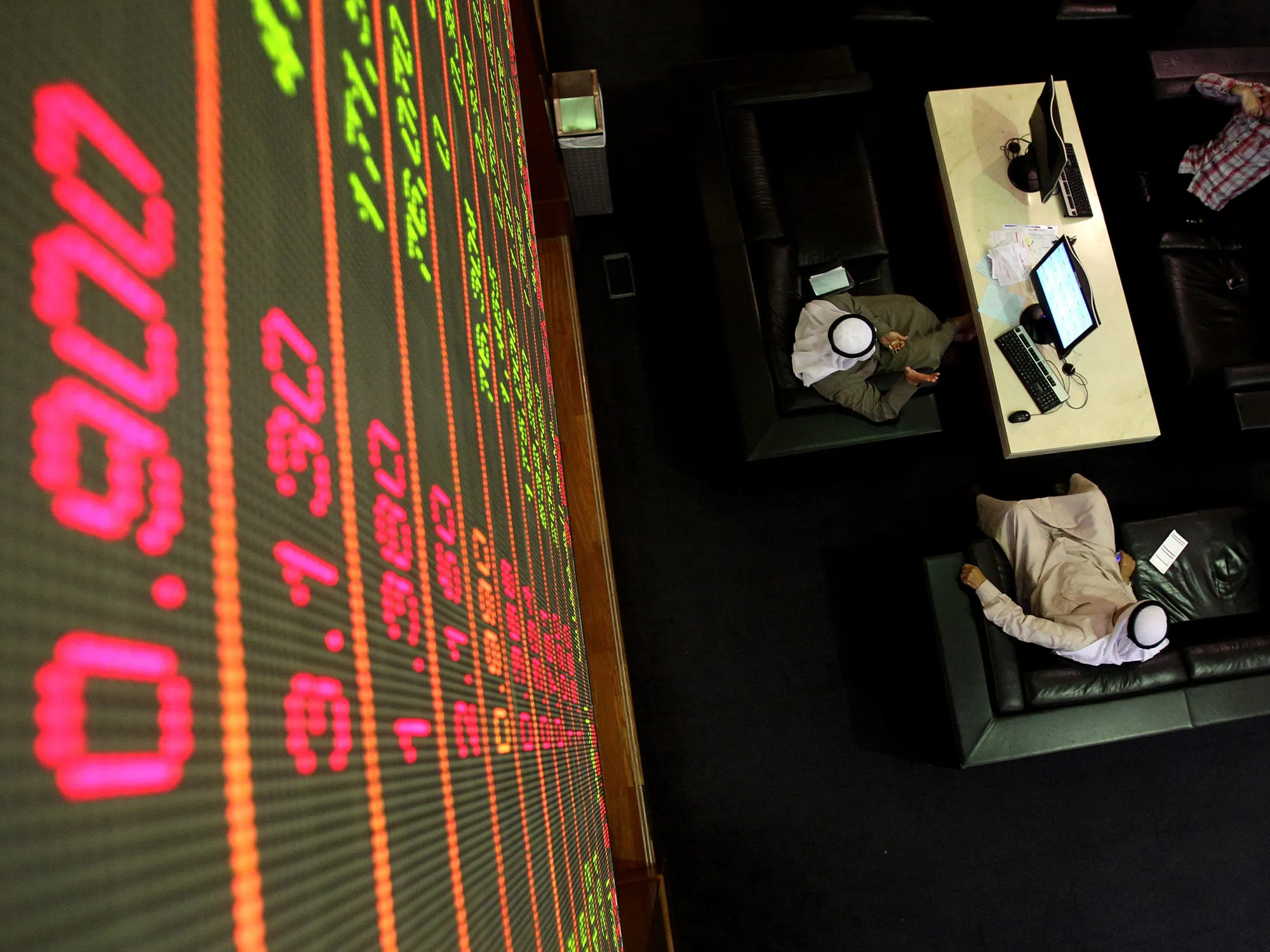 Emirati men sit under a stock market scr