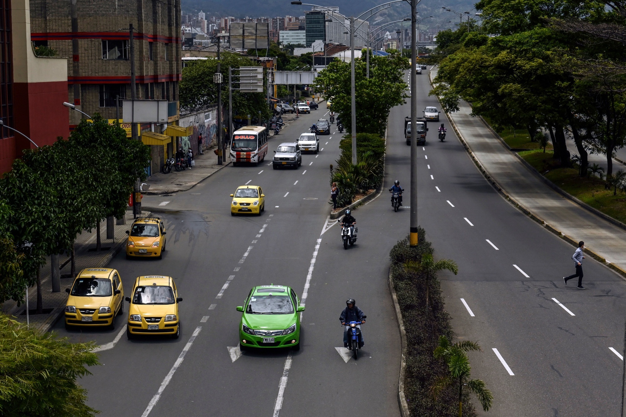 An electric taxi (C, green) drives along a street in Medellin, Colombia, on September 19, 2019.&nbsp;