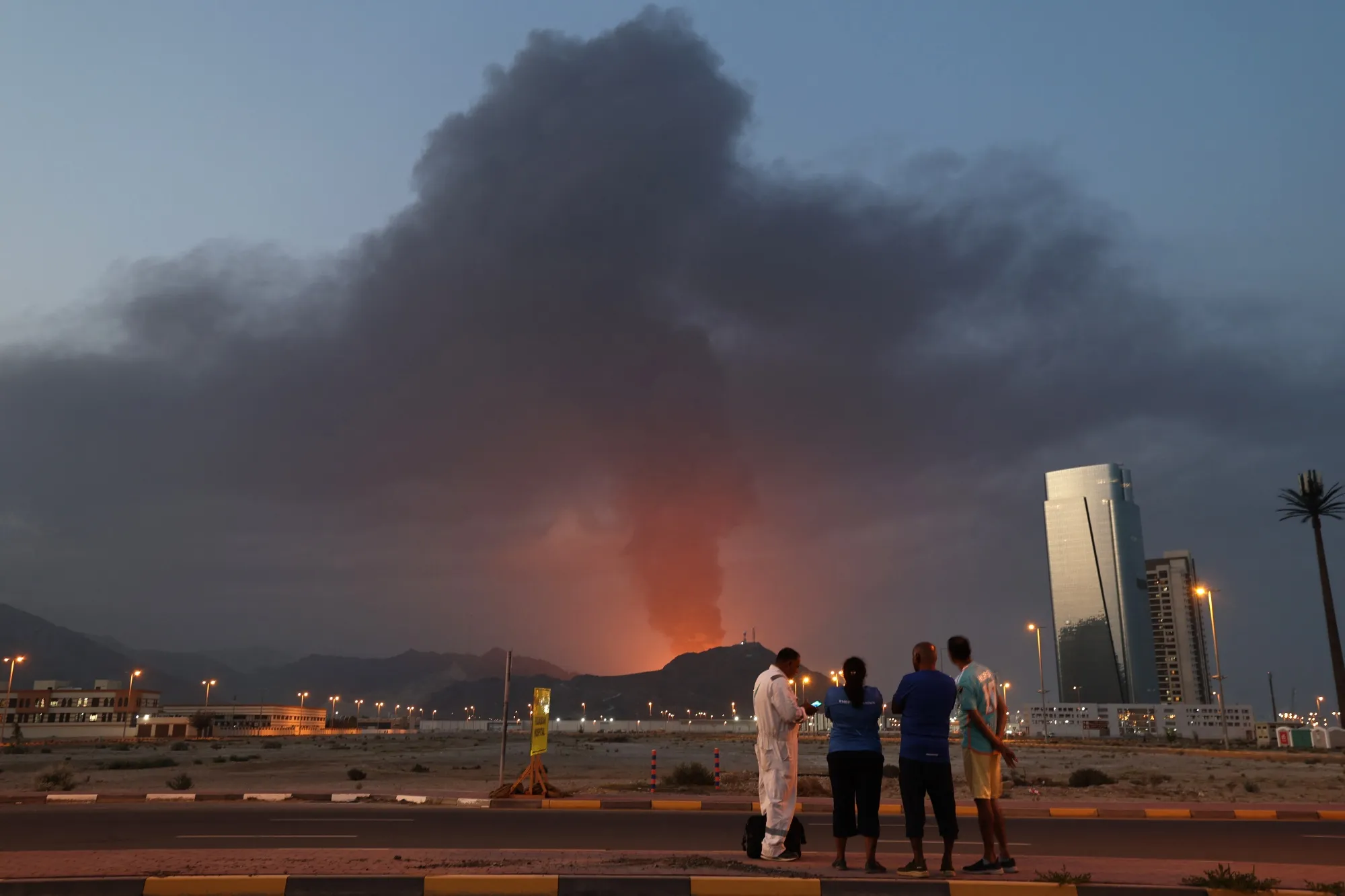 Foreign workers look as a tall plume of black smoke ascends following an explosion in the Fujairah industrial zone in the UAE on March 3, 2026.