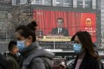 Pedestrians walk past a screen showing a live news broadcast of Chinese Premier Li Keqiang speaking in Beijing, China