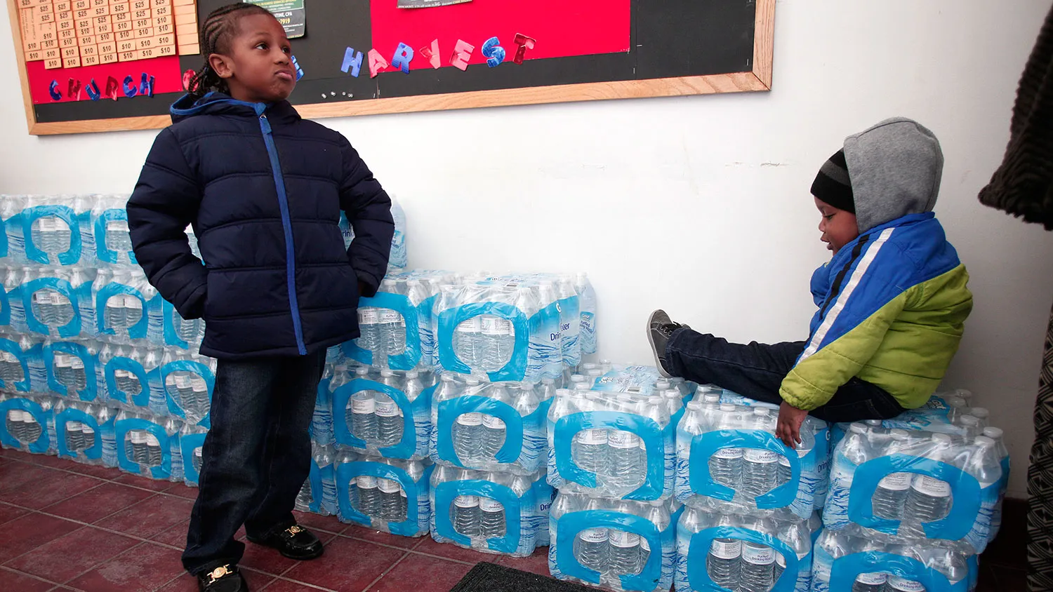 Justin Roberson (left), age 6, and Mychal Adams, age 1, wait on a stack of bottled water at a rally where the Rev. Jesse Jackson was speaking about about the water crisis on Jan. 17, 2016 in Flint, Michigan.
