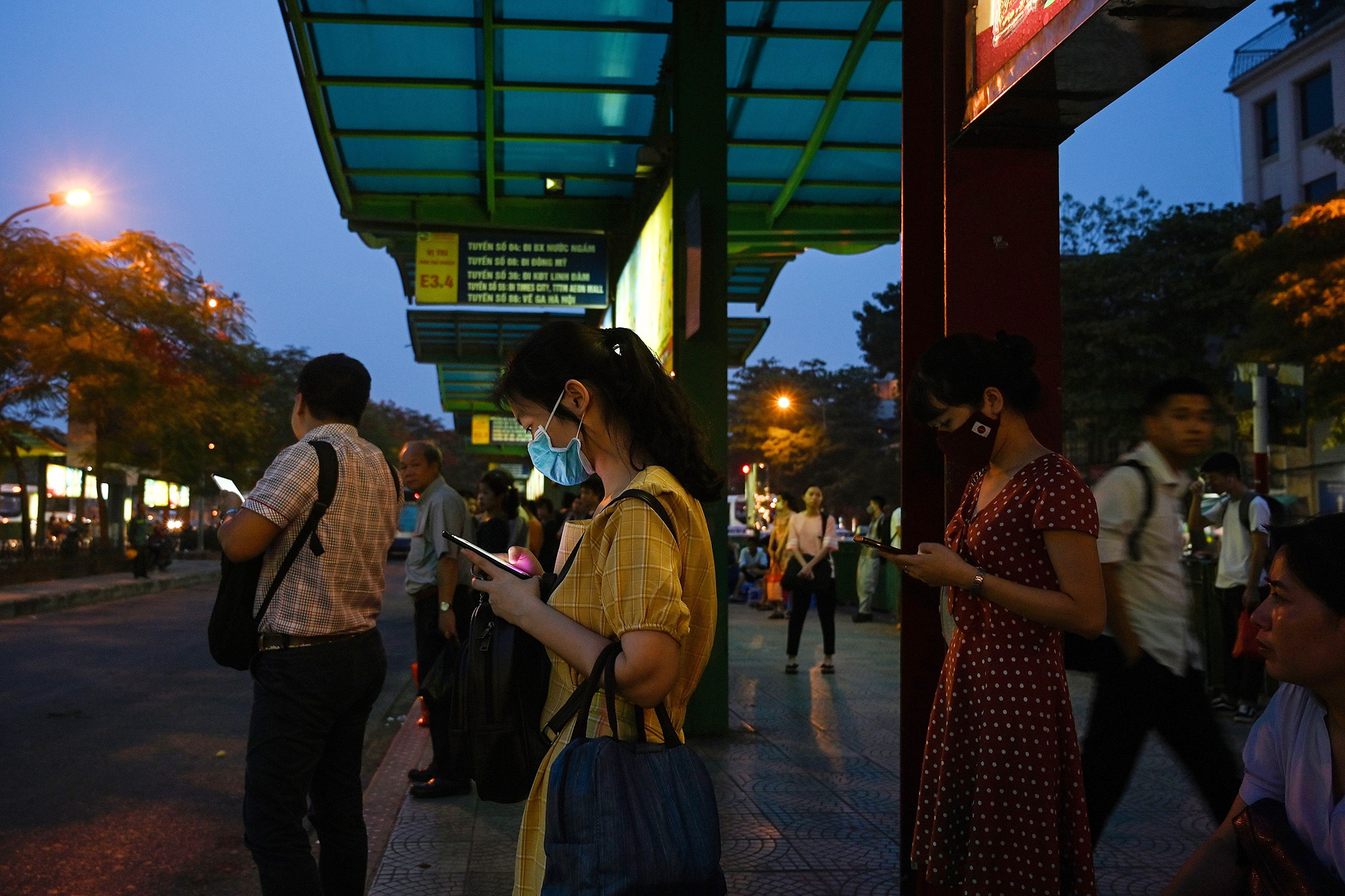 People use their smartphones while waiting at a bus stop in Hanoi.&nbsp;