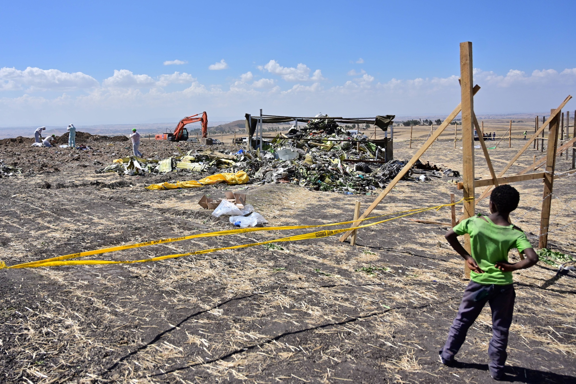A boys look as forensic investigators comb the ground for DNA evidence near a pile of airplane debris at the crash site of an Ethiopian airways operated Boeing 737 MAX aircraft on March 16, 2019.