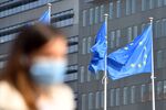 A pedestrian wearing a protective face mask passes European Union&nbsp;flags