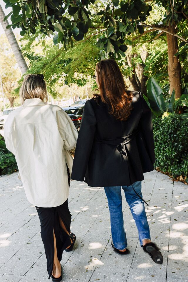 Two women wearing blazers walk along a street of the Design District. 