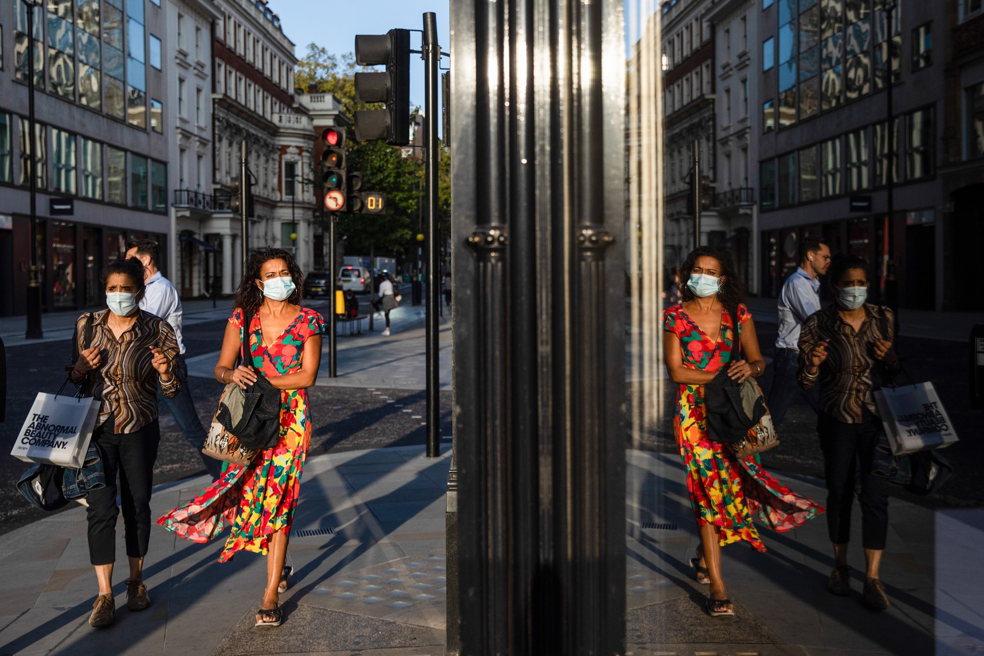 A shop window reflects pedestrians in protective masks on New Bond Street in central London, UK