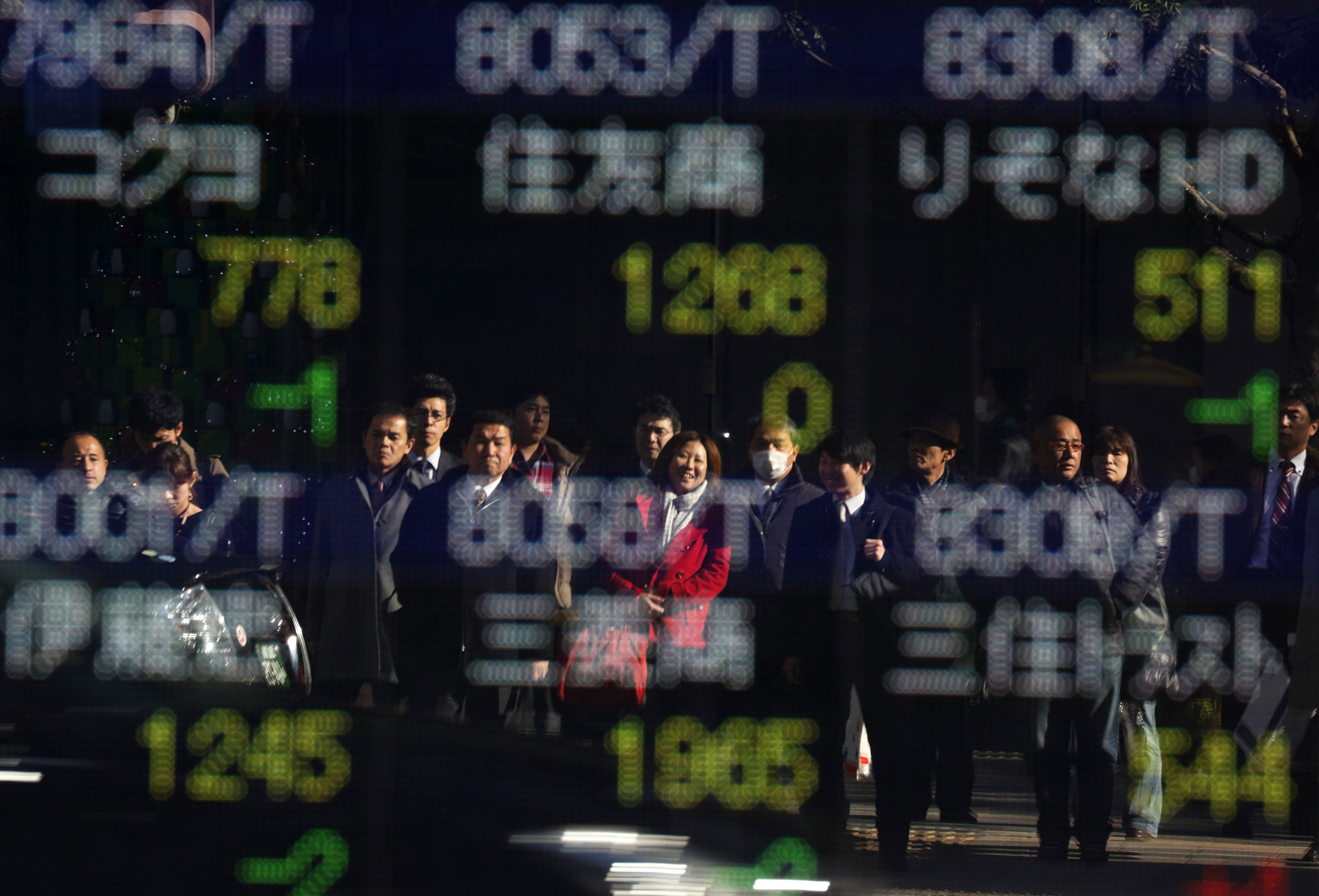 Pedestrians are reflected in a window in front of a stock board outside a securities firm in Tokyo.
