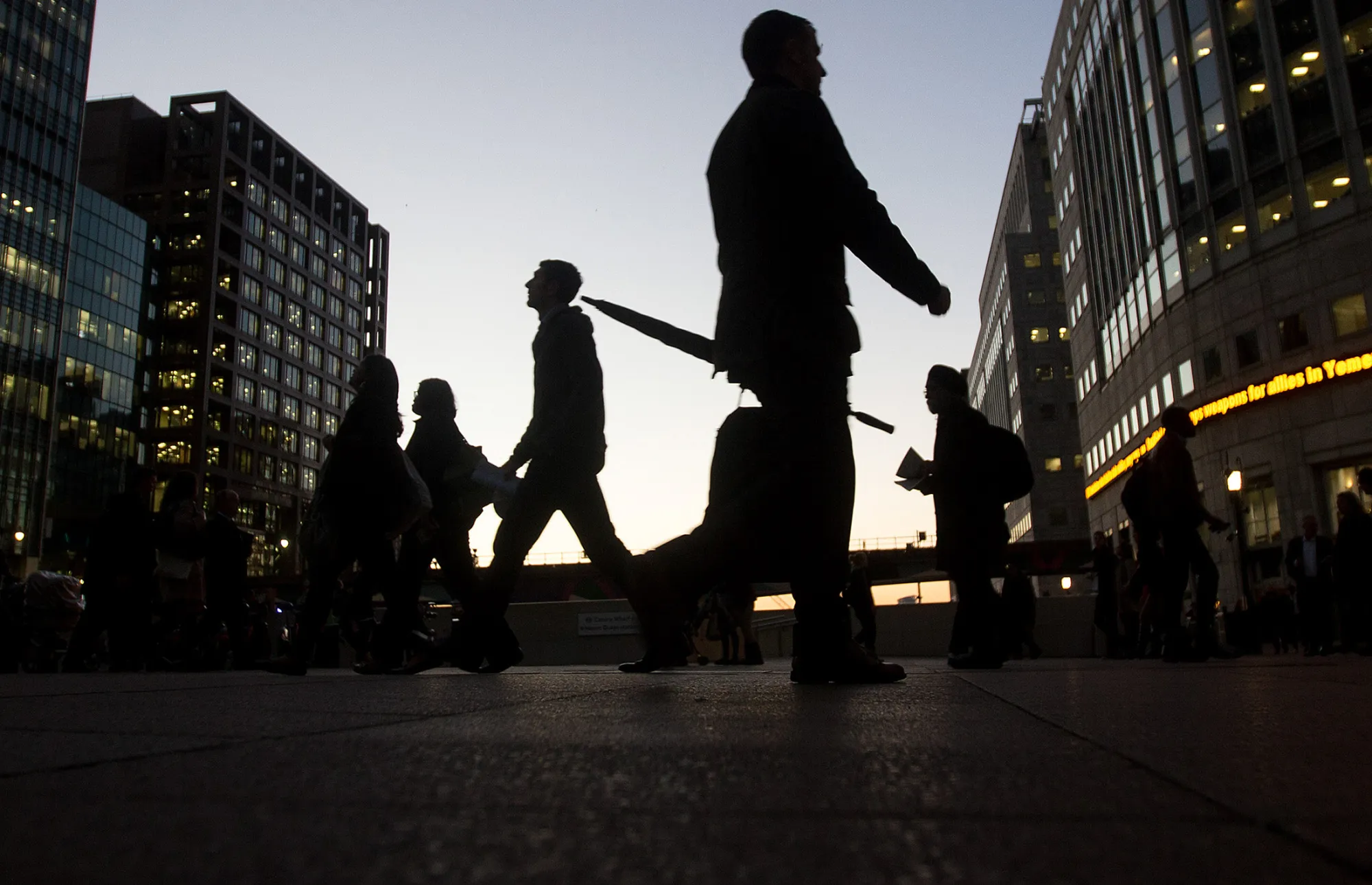 Commuters walk past the JP Morgan, left, and Thomson Reuters Corp., right, buildings illuminated at night in the Canary Wharf business, financial and shopping district of London, U.K., on Wednesday, Oct. 28, 2015.
