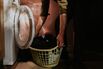 A man holds a washing basket in a utility room, prior to loading a modern washing machine within a utility room.