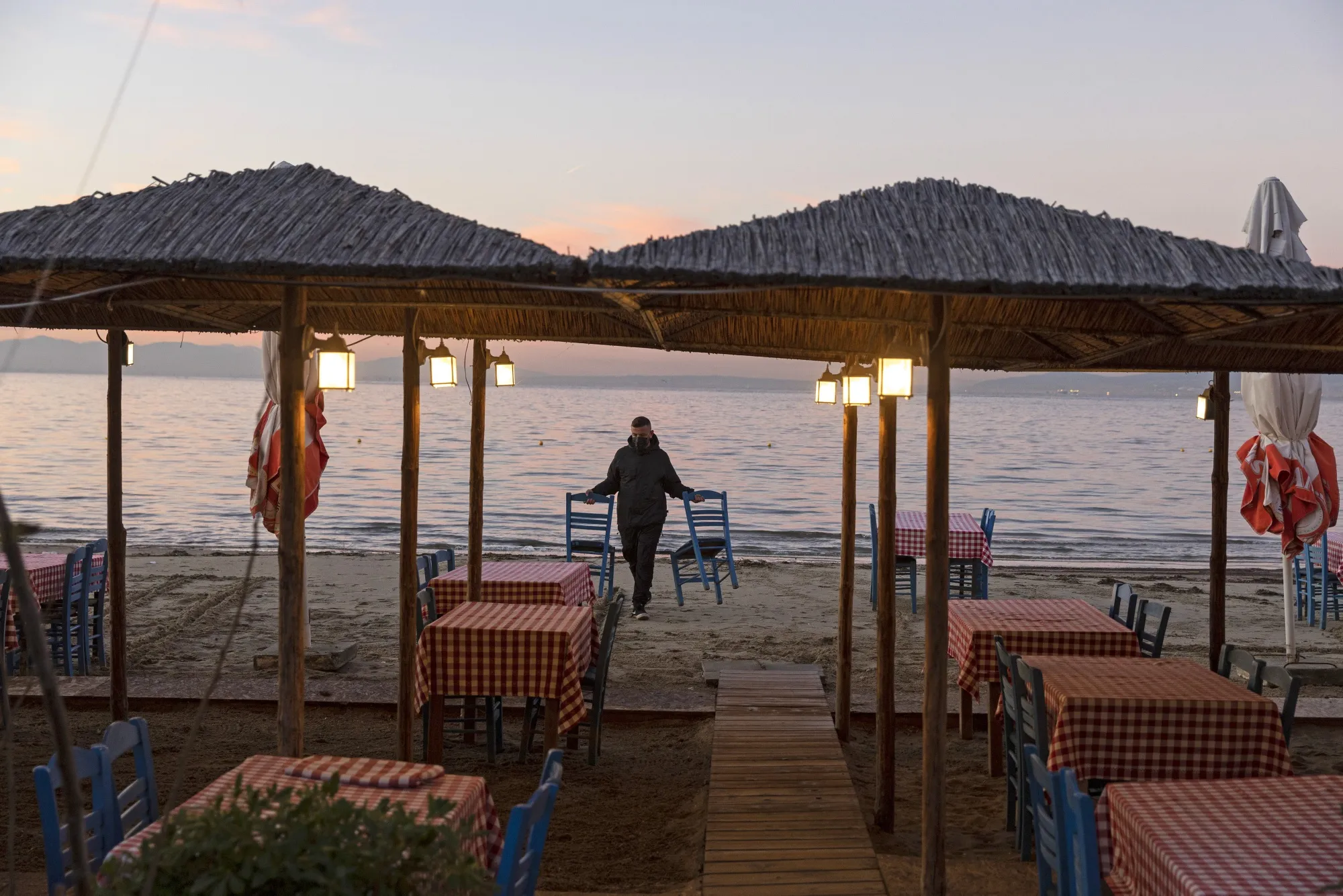 A waiter collects chairs from the beach at an empty seaside restaurant in Thessaloniki, Greece.