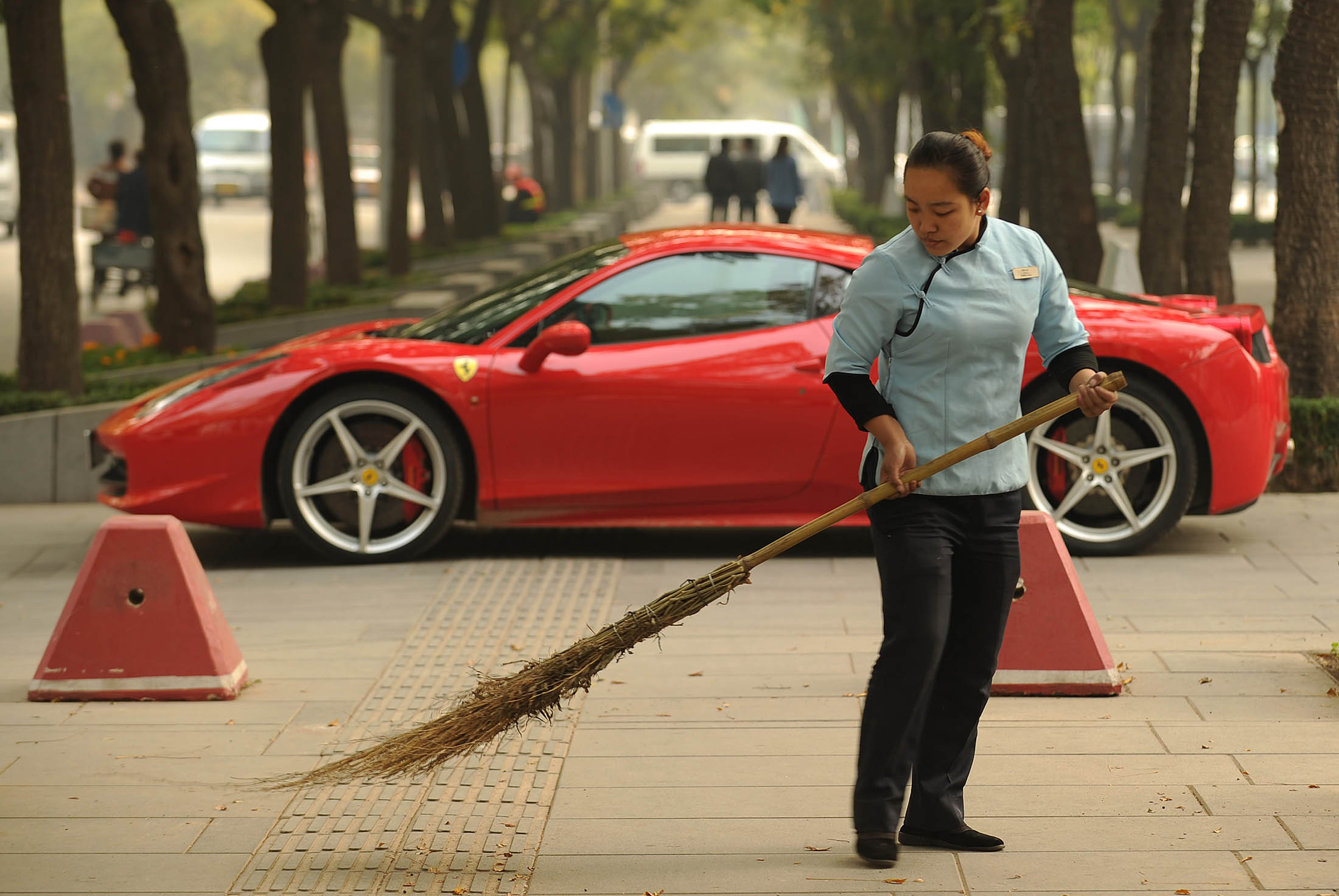 A woman sweeps leaves in front of a new Ferrari 458 Italia in Beijing on October 28, 2011. The head of the European bail-out fund dampened hopes October 28 that China Would come to a debt-stricken EU's rescue, but left the door open for a deal with the world's second-biggest economy. AFP PHOTO / Peter PARKS (Photo credit should read PETER PARKS/AFP/Getty Images)

