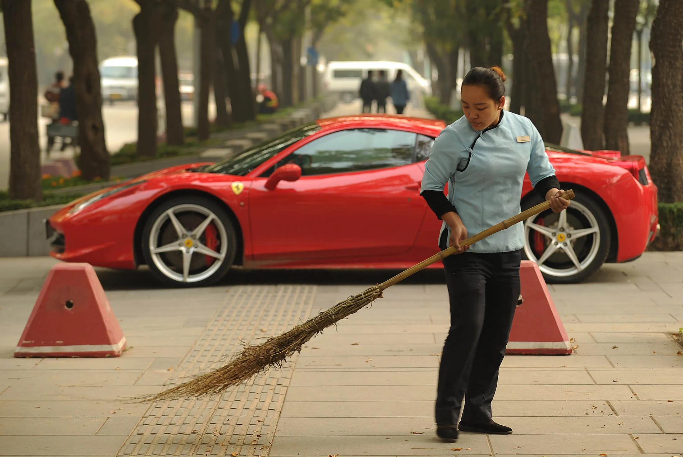 A woman sweeps leaves in front of a new Ferrari 458 Italia in Beijing on October 28, 2011. The head of the European bail-out fund dampened hopes October 28 that China Would come to a debt-stricken EU's rescue, but left the door open for a deal with the world's second-biggest economy. AFP PHOTO / Peter PARKS (Photo credit should read PETER PARKS/AFP/Getty Images)
