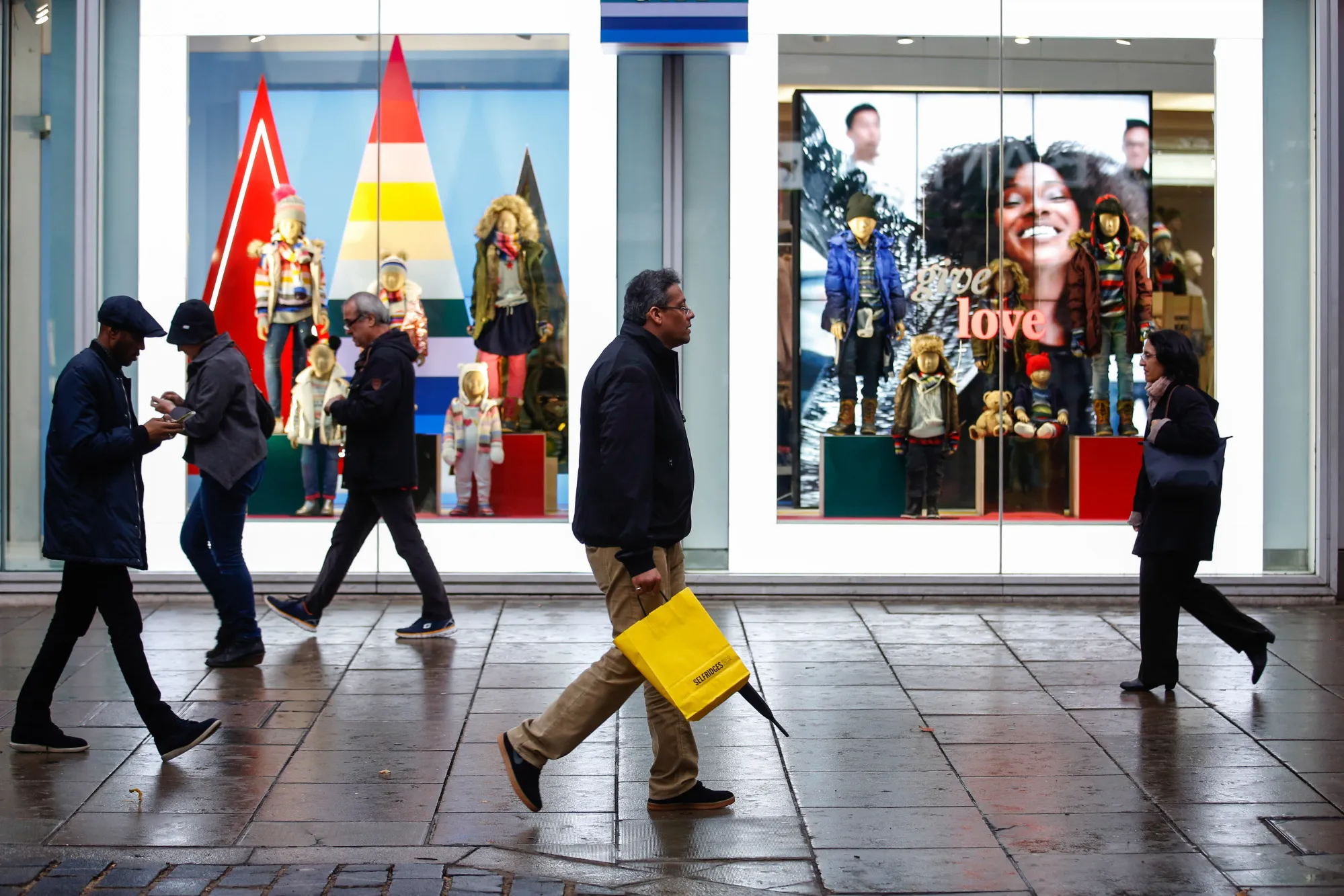 Shoppers passes a Gap Inc. fashion retail shop while walking along on Oxford Street in central London, U.K., on Tuesday, Nov. 7, 2017. U.K. retail sales fell the most in seven months in October, indicating continued caution among consumers just weeks before the crucial Christmas shopping season.