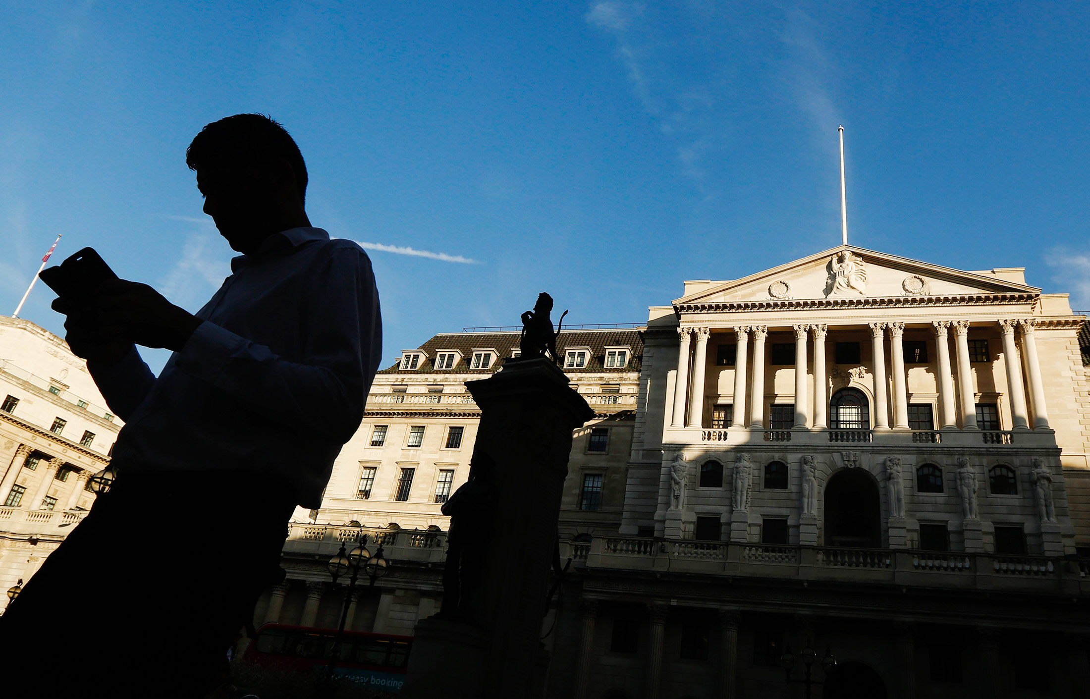 A man looks at his smartphone as he walks past the Bank of England (BOE) in the City of London, U.K., on Tuesday, Sept. 13, 2016. BOE officials announce their next interest rate decision on Thursday, when they are forecast to keep policy unchanged as they assess the outlook for the economy since the Brexit vote.
