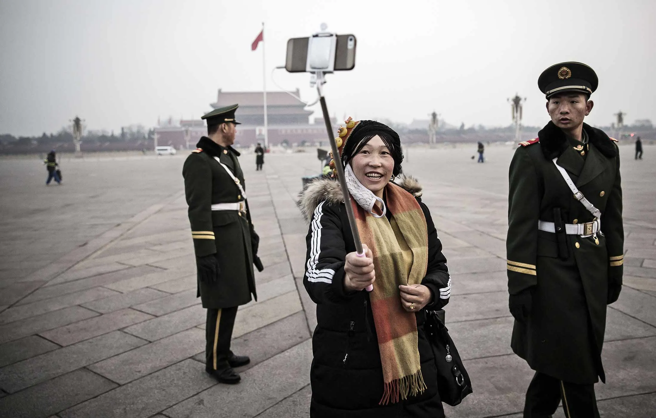 A visitor takes a selfie photograph with paramilitary police officers using a smartphone on a monopod following the daily national flag-raising ceremony at Tiananmen Square in Beijing, China, on Thursday, March 3, 2016.
