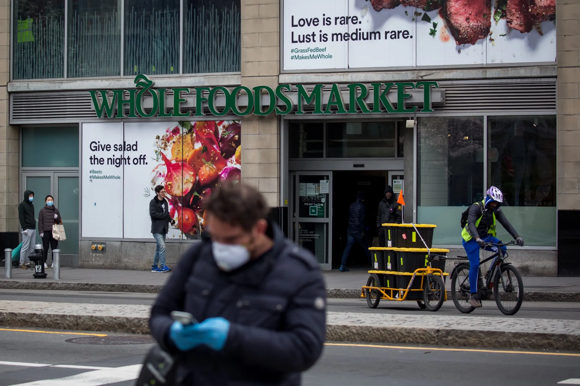 People wait in line outside a Whole Foods Market Inc. store as a delivery worker pedals a bike in New York, on&nbsp;March 31.