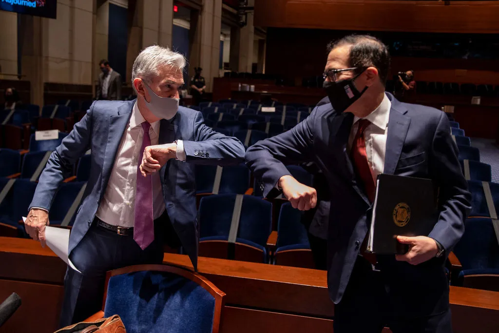 Federal Reserve Chairman Jerome Powell (left) has a mask and greeting game that are up to date. His job description, not so much.