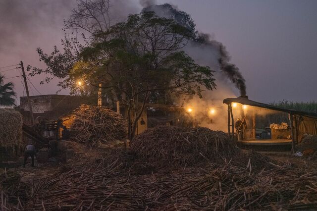 Workers operates as smoke rises from a jaggery plant, in Muzaffarnagar District, Uttar Pradesh, India, on Monday, Nov. 21, 2022.