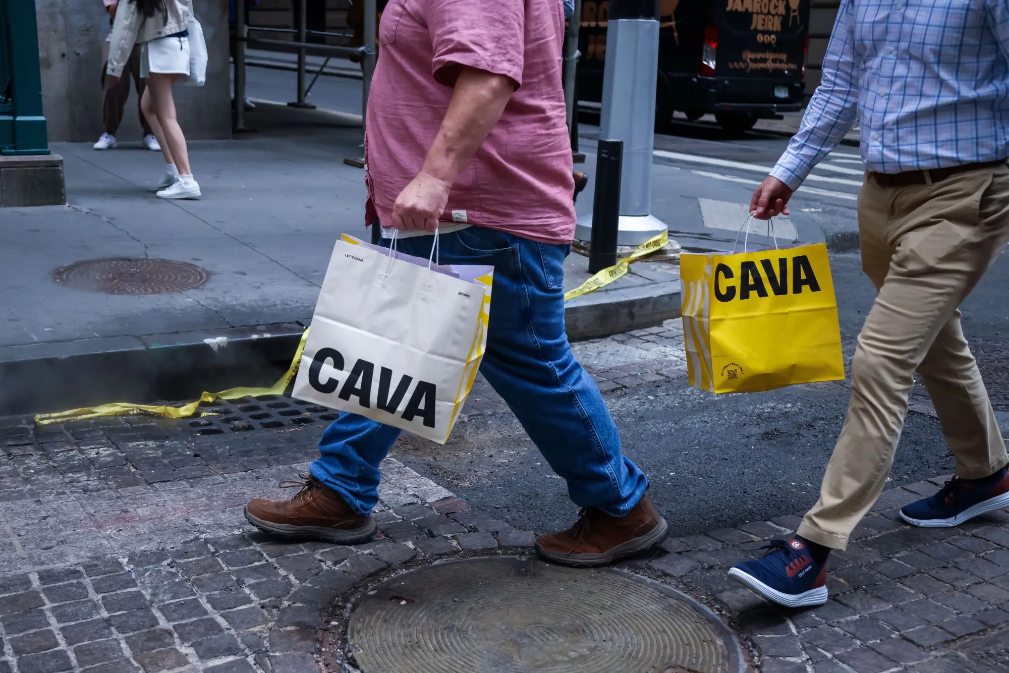 Pedestrians carry Cava bags along Wall Street near the New York Stock Exchange (NYSE) in New York, US.