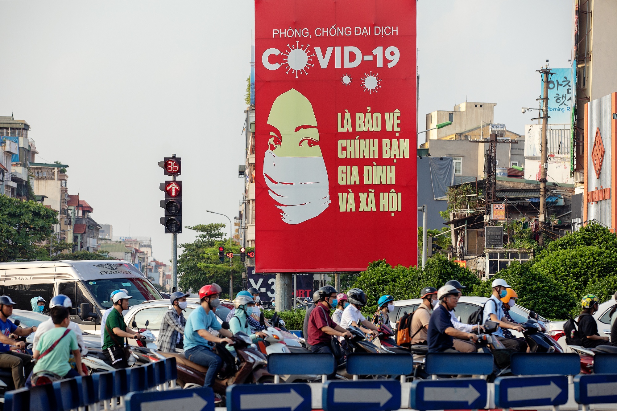 Motorcyclists ride past a public information hoarding about coronavirus displayed in Hanoi, Vietnam.