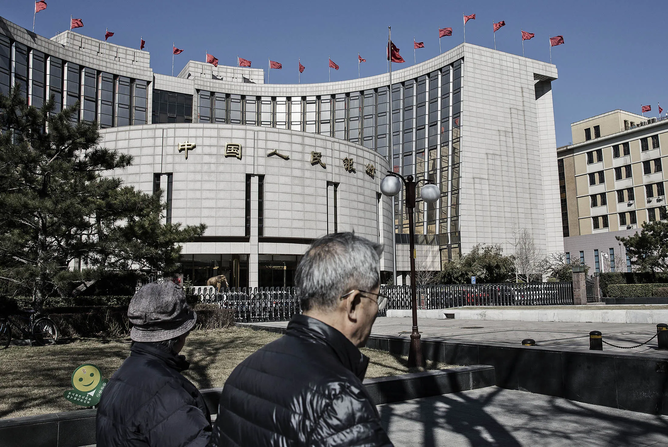 Pedestrians walk past the People's Bank of China (PBOC) headquarters in Beijing, China, on Monday, March 7, 2016. Chinese small-cap stocks rallied after Premier Li Keqiang failed to mention a planned shift to a more market-based system for initial public offerings, a reform seen luring funds from existing equities.
