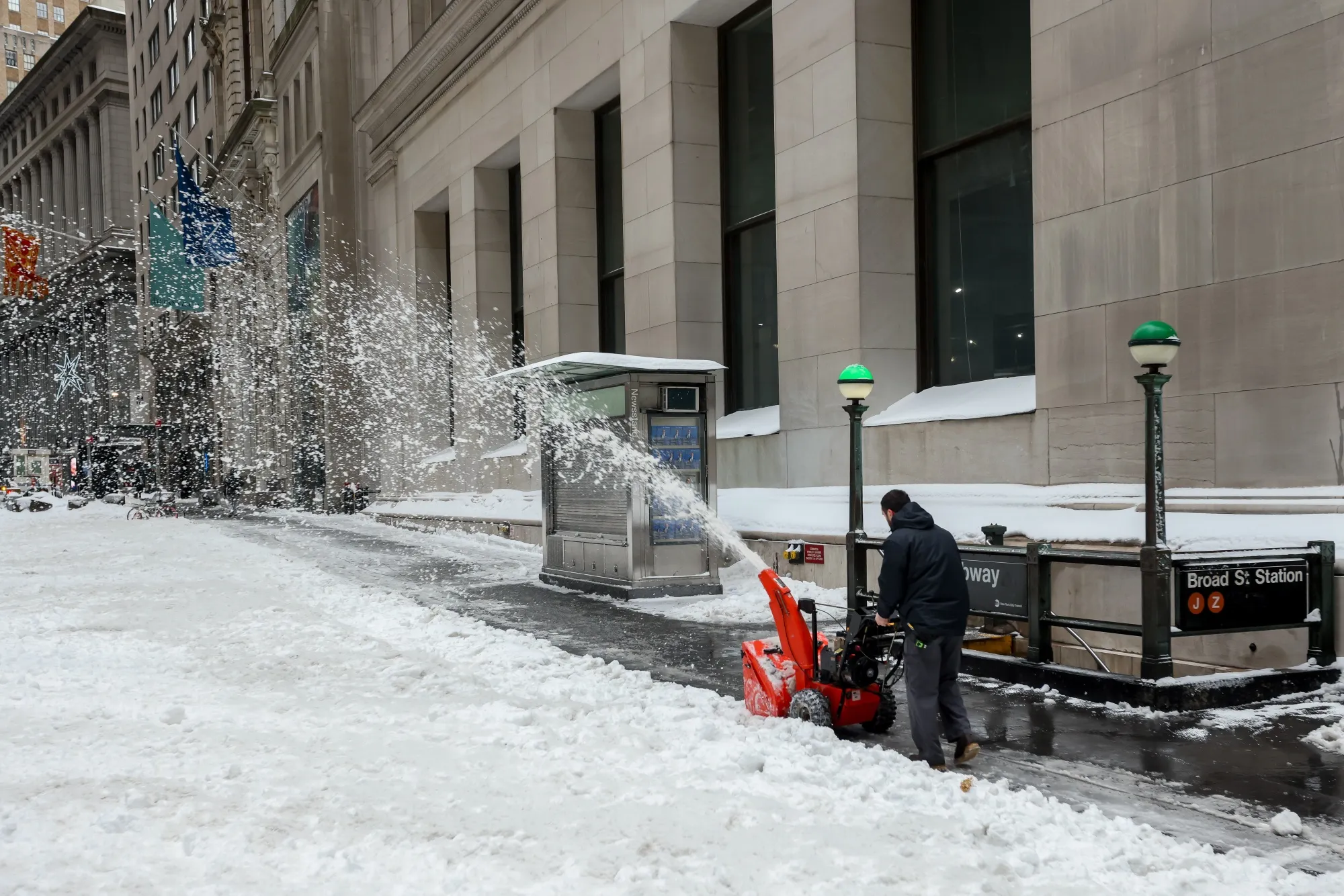 A worker blows snow on a sidewalk.