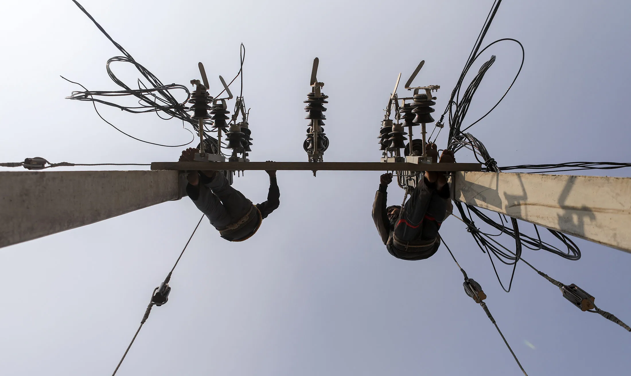 Workers connect electricity cables to a transmission pole during an implementation program by the Rural Electrification Corp. in the village of Manpur Kulchaura, Uttar Pradesh, India, on Sunday, Jan. 15, 2017.
