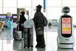 Travelers wearing protective masks stand next to a robot at Incheon International Airport in Incheon, South Korea.