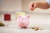 two years old child sitting on the floor and putting a coin into a piggybank