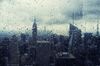 The New York City skyline is seen blurred through a raindrop covered plexi glass.