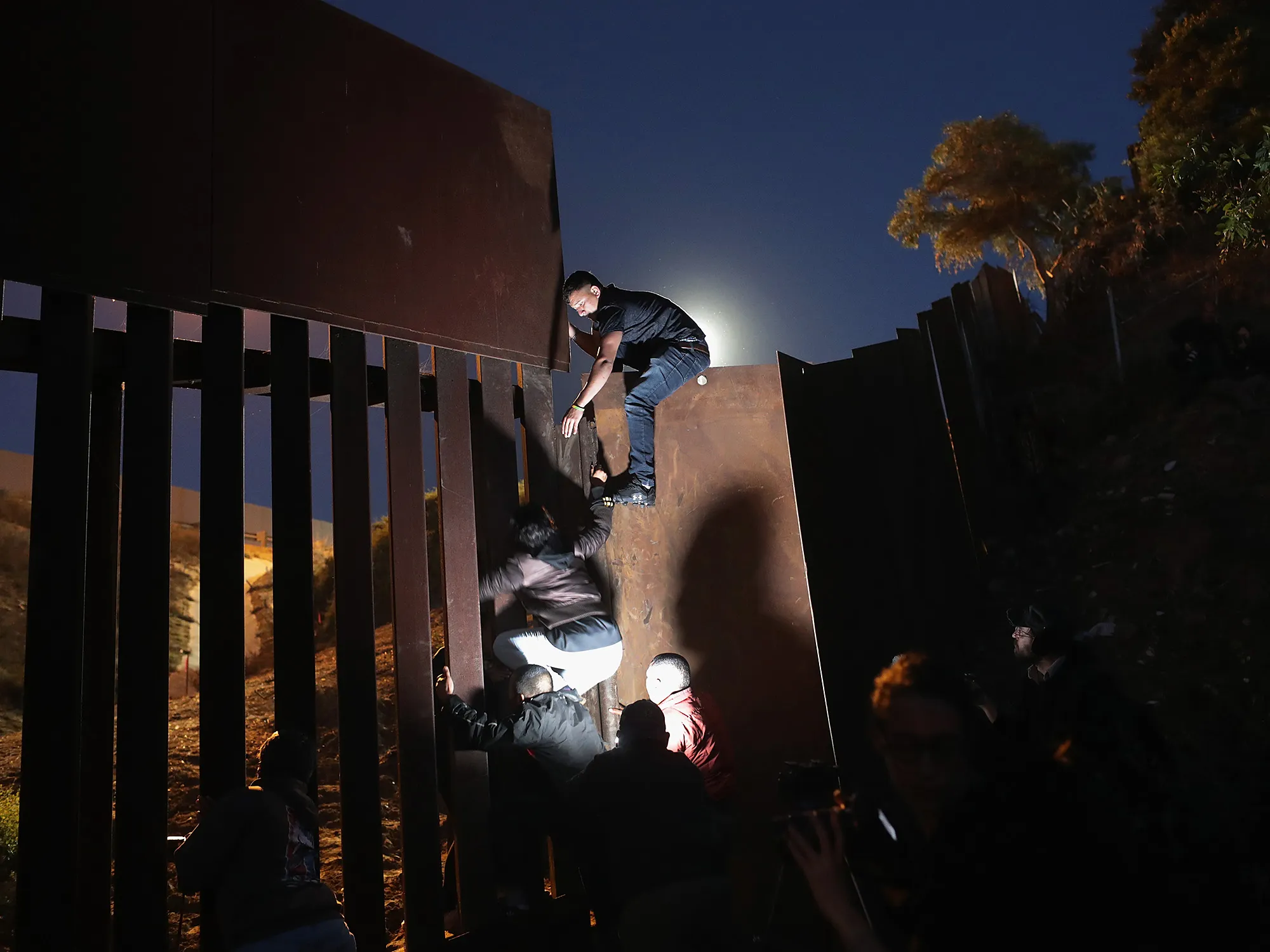 People climb over the U.S.-Mexico border fence on Dec. 3, 2018 while crossing into San Diego,&nbsp;from Tijuana, Mexico.