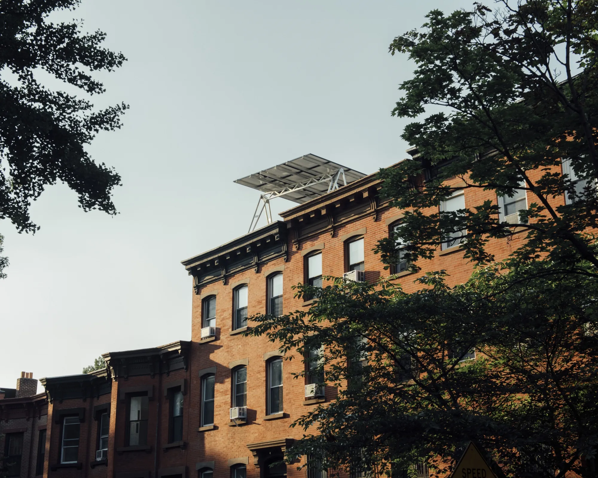 Rooftop solar panels peek out&nbsp;over the facade of a row house in Brooklyn.&nbsp;